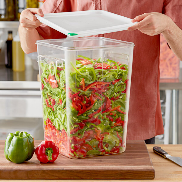 A person using a white Araven square container to hold cut green bell peppers.