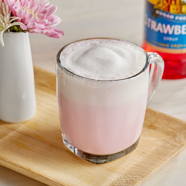 A glass mug of pink foam with Torani Sugar-Free Strawberry Flavoring Syrup and a pink flower.