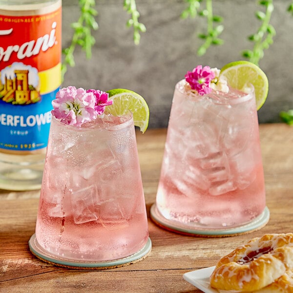 Two glasses of pink drinks with flowers and limes using Torani Elderflower Flavoring Syrup.