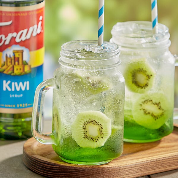 A glass jar of lemonade with a straw and kiwi slices in it.