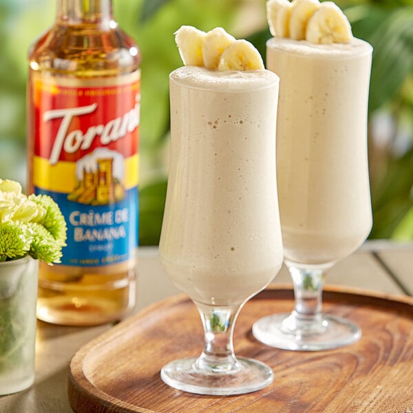Two glasses of milkshakes made with Torani Creme de Banana flavoring syrup with bananas on top.