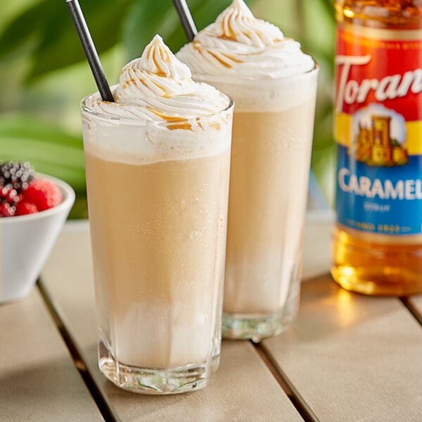 Two glasses of iced coffee with whipped cream and Torani Caramel Flavoring Syrup on a table.