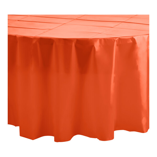 A table covered in orange Table Mate round plastic tablecloths with a ruffled edge.