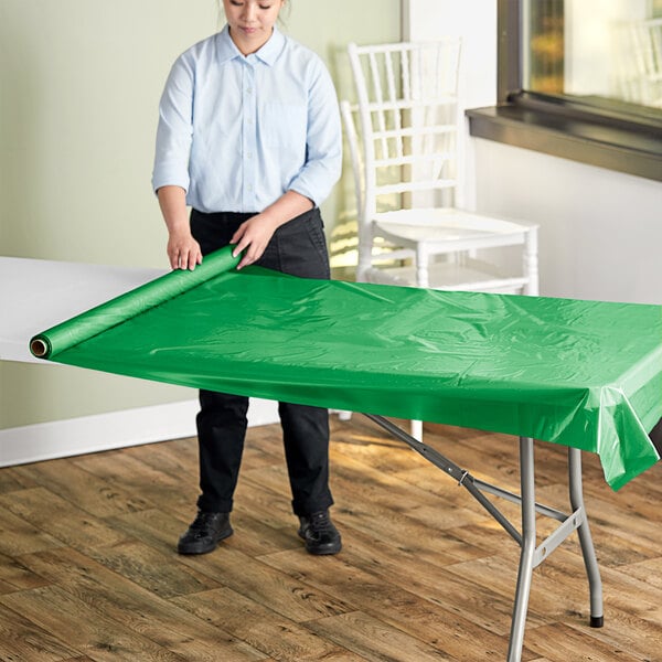 A person rolling a green plastic sheet onto a table.
