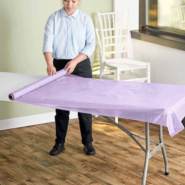 A woman rolling a lavender plastic sheet onto a table.