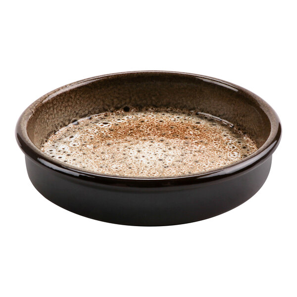A brown terracotta bowl with a brown rim filled with brown liquid.