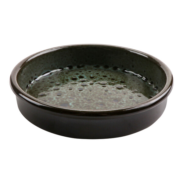 A terracotta bowl with a black and green glaze filled with liquid.
