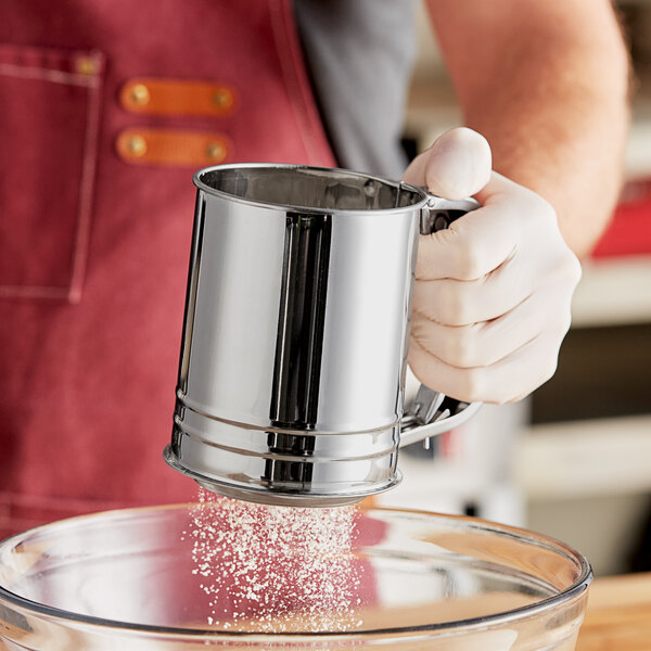 A person using a Choice stainless steel trigger action sifter to pour powdered sugar into a bowl.