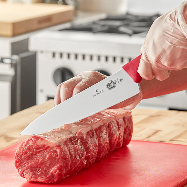 A person using a Victorinox chef knife to cut meat on a cutting board.