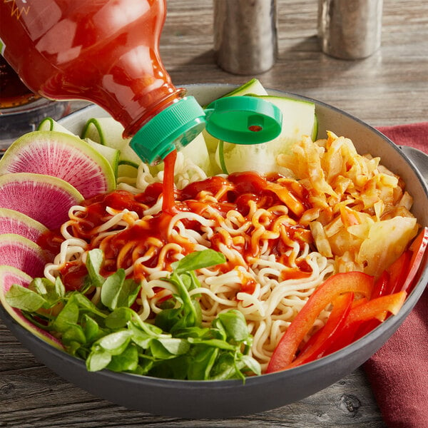 A bowl of noodles with Sriracha sauce being poured over it.