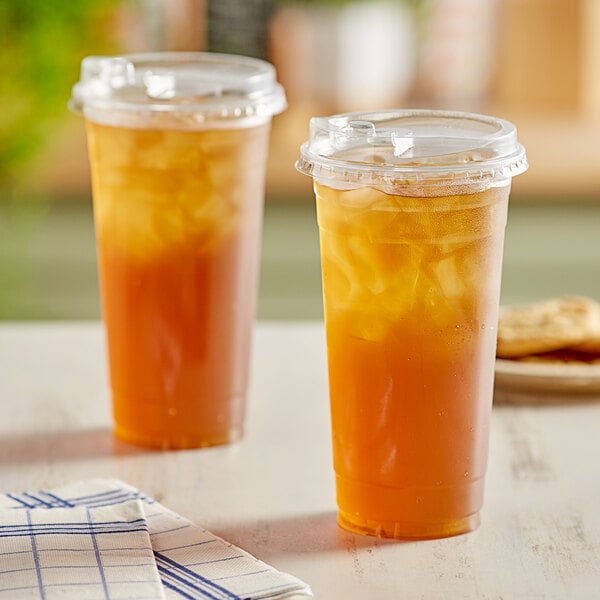 Two Choice clear plastic cups of iced tea with a strawless sip lid on a table.