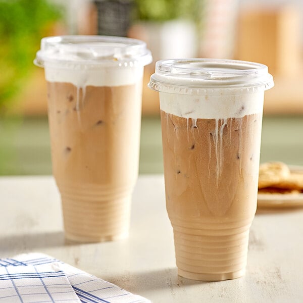 Two Choice clear plastic cups of iced coffee with whipped cream and extra wide lids.