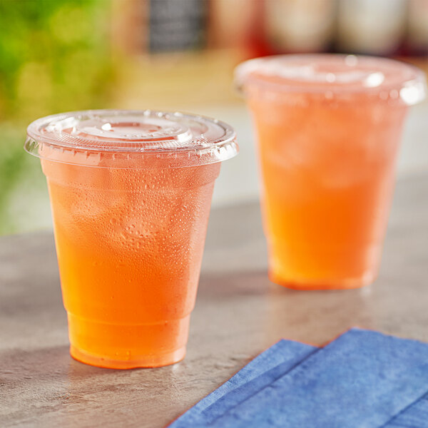Two Choice clear plastic cups filled with orange juice on a table with blue napkins.