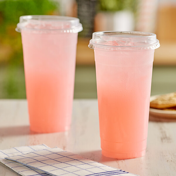 Two Choice clear plastic cups of pink liquid on a table.