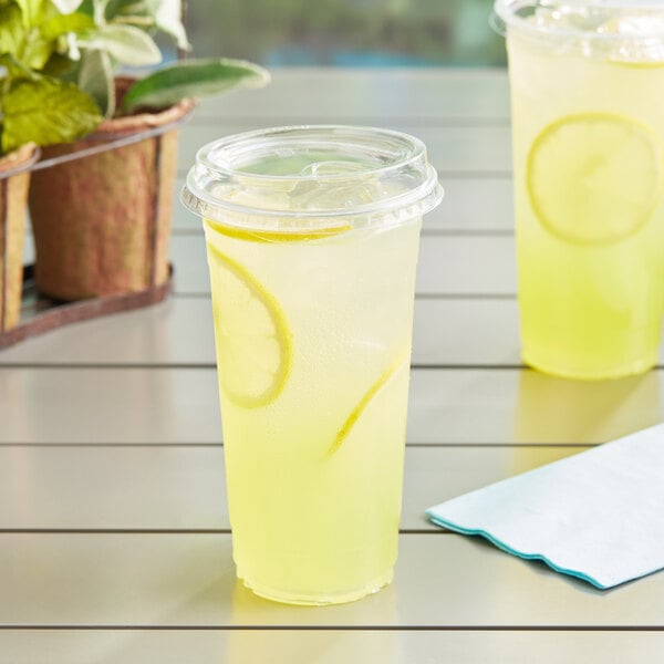 Two Choice clear plastic cups of lemonade with a lemon slice on a table.