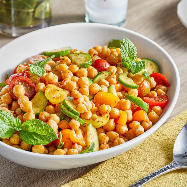 A bowl of chickpeas with vegetables on a table.