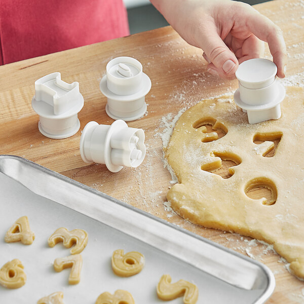 A person using Ateco number plunger cutters to cut out cookie dough shapes.