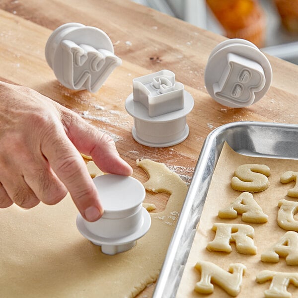 A person using an Ateco plastic alphabet cookie cutter to cut out letters for cookies.