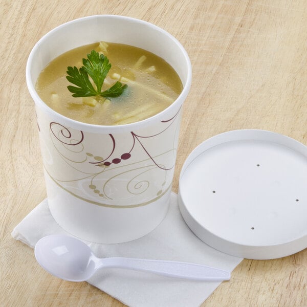 A Solo Symphony paper soup cup filled with soup and a white lid with a spoon on the side.