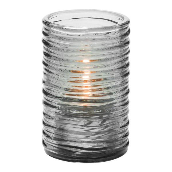 A Hollowick Typhoon smoke glass cylinder candle holder with a lit candle.