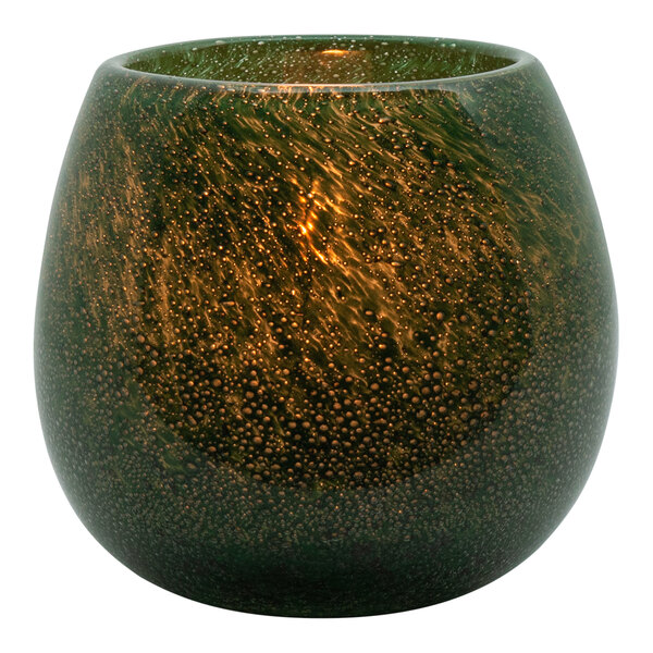 A close up of a green and gold Hollowick art glass candle holder with a lit candle inside.
