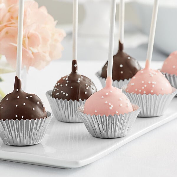 A chocolate covered cake pop in a silver Enjay mini baking cup on a white plate.