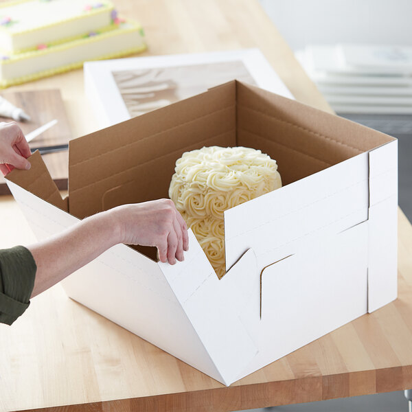 A person opening a white Enjay Flexbox with a cake inside.