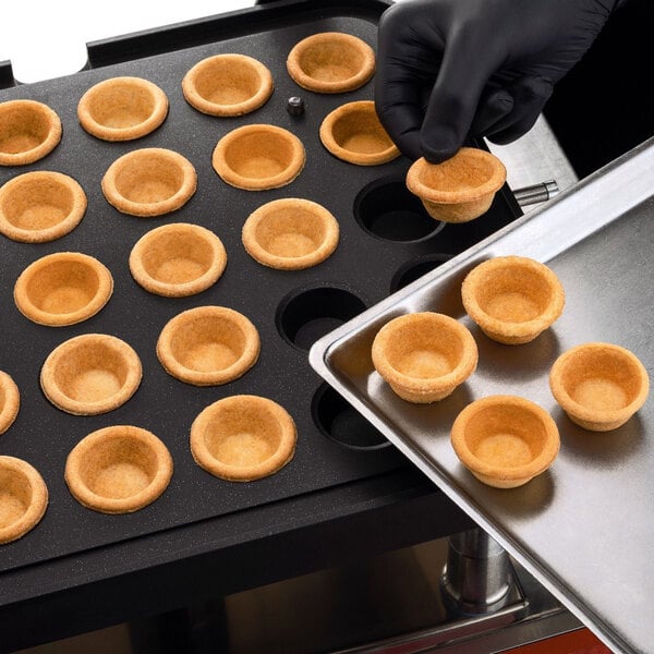 A gloved hand using a Pavoni Cookmatic to make small round brown pastries.
