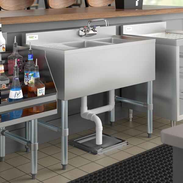 A Regency stainless steel underbar sink with left drainboard on a counter with bottles of liquid in it.