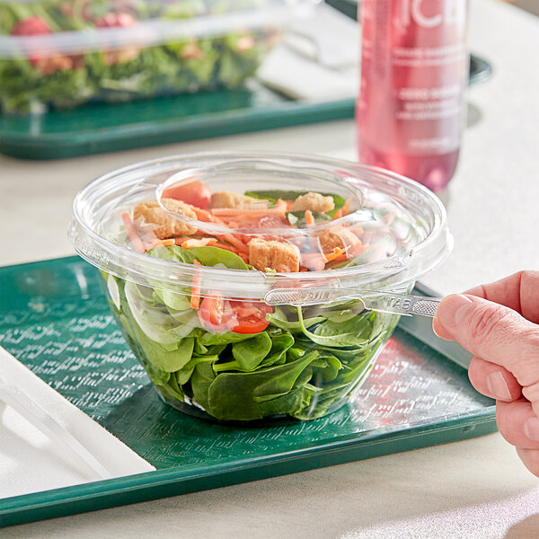 A hand holding an Inline Plastics Safe-T-Fresh plastic container filled with salad.
