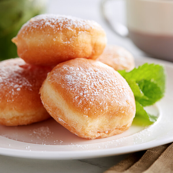A plate of White Toque plain mini beignets with powdered sugar on them.