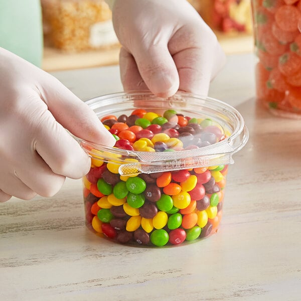 A person holding a Inline Plastics Safe-T-Fresh plastic container filled with colorful candies.