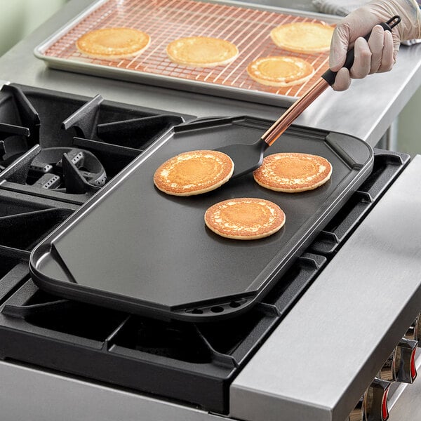 A person cooking pancakes on a Nordic Ware reversible griddle.