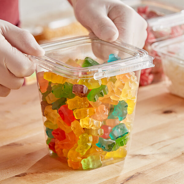 A person holding a plastic Inline Plastics container of gummy bears.