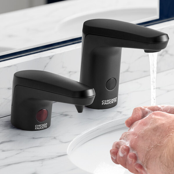 A person using a Chicago Faucets matte black touchless soap dispenser to wash their hands.