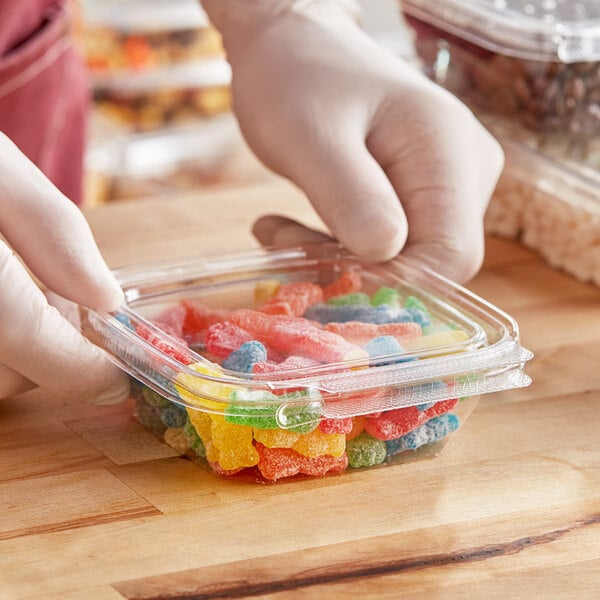 A person in gloves holding a Inline Plastics plastic container of colorful gummy candies.