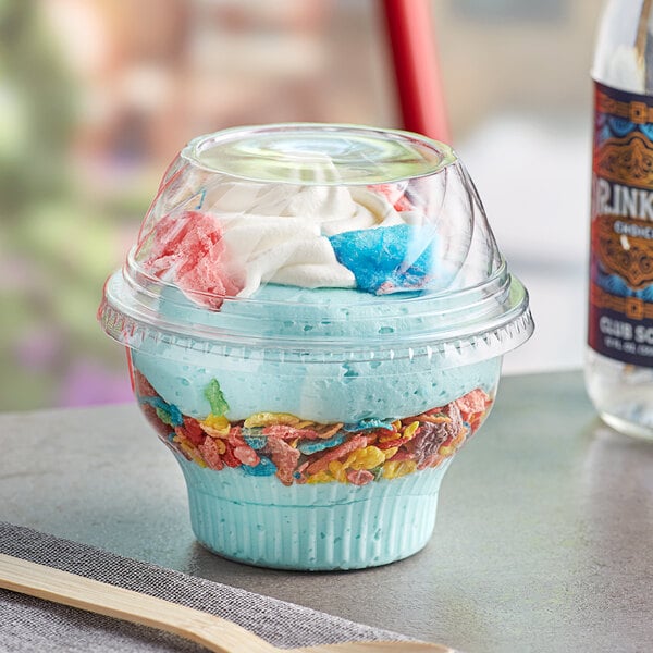 A clear plastic cup of blue ice cream with cereal and whipped cream.