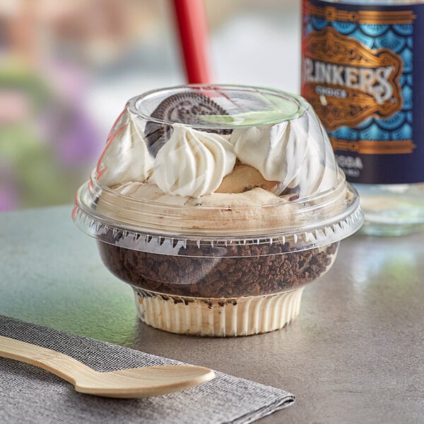 A Choice clear plastic dessert cup of ice cream with whipped cream, cookies, and a wooden spoon.