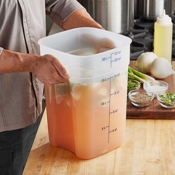 A man holding a Cambro CamSquares container of liquid in a professional kitchen.