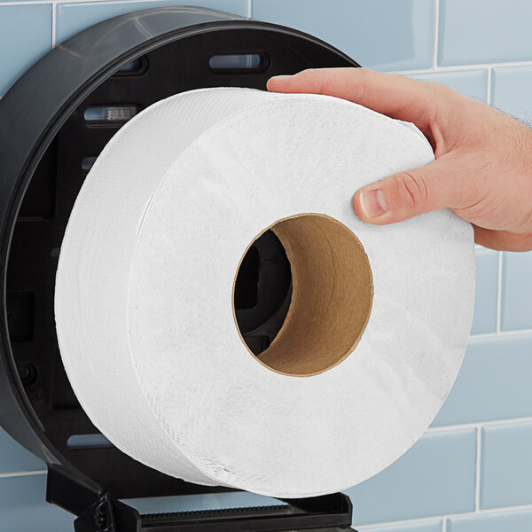 A hand holds a Morcon jumbo toilet paper roll in front of a toilet.