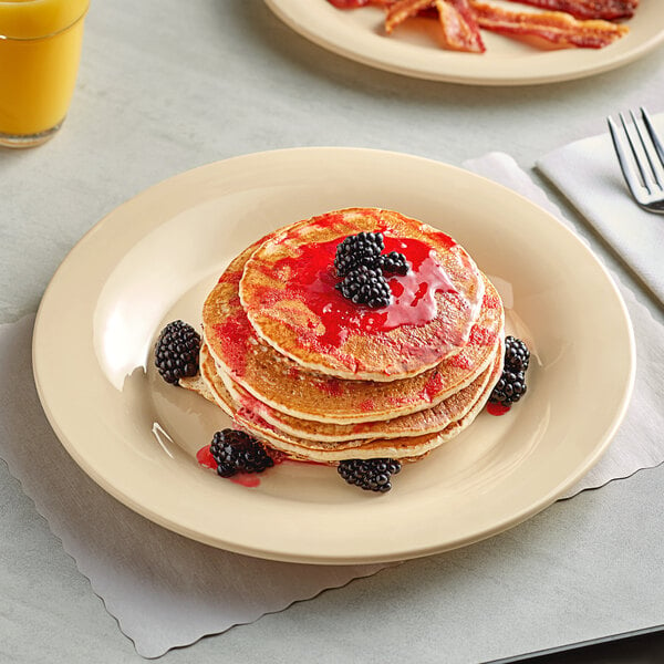 A stack of pancakes with berries and syrup on an Acopa Foundations tan melamine plate.