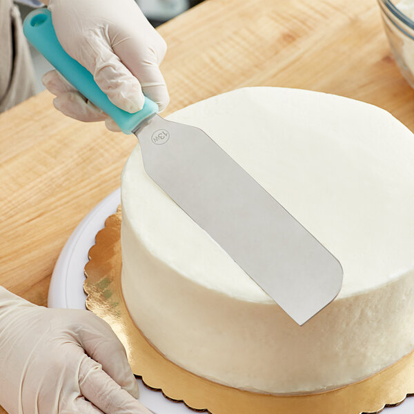 A person using a Wilton straight wide baking spatula to cut a cake.