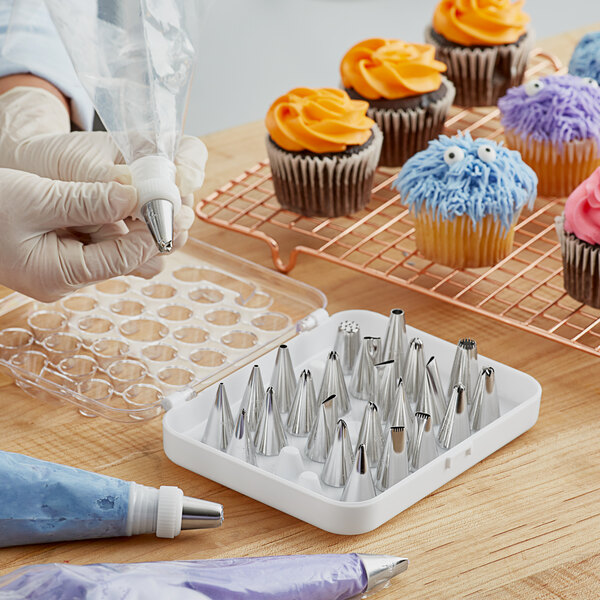 A hand using a Wilton stainless steel piping tip to decorate a cupcake.