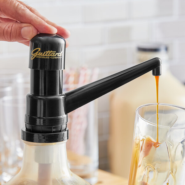 A hand using a black Guittard sauce pump to pour liquid into a glass.
