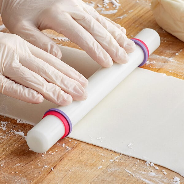 A person wearing gloves rolling out dough with a Wilton plastic French rolling pin.