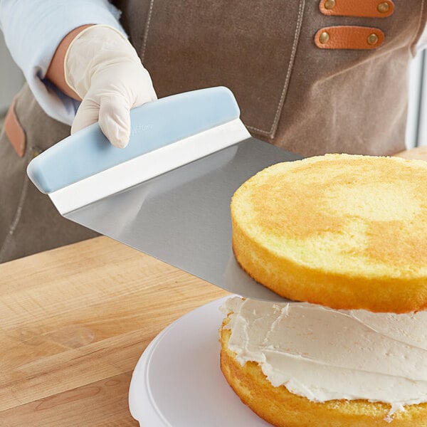 A person wearing gloves using a Wilton stainless steel cake lifter to serve a cake.