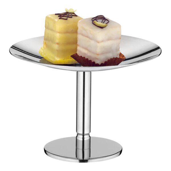 A WMF by BauscherHepp stainless steel pastry display stand holding small yellow cakes.