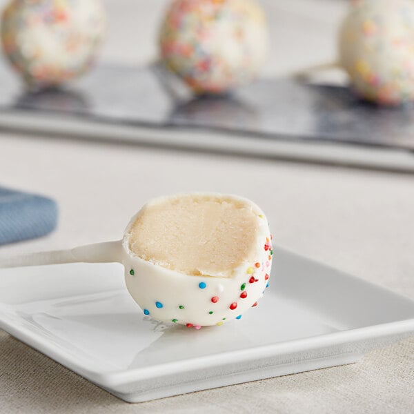 A Coco Bakery birthday cake pop with colorful sprinkles on a white plate.