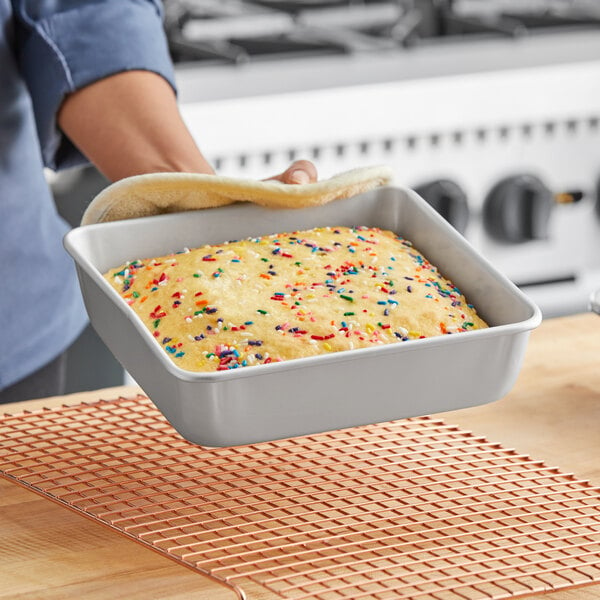 A person holding a square cake in a Wilton cake pan with sprinkles on top.