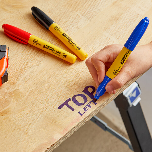 A hand using an Avery Marks-A-Lot yellow permanent marker to write on a wood surface.